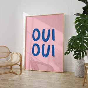 May include: A pink and blue wall art print with the text "OUI OUI" in bold blue letters.