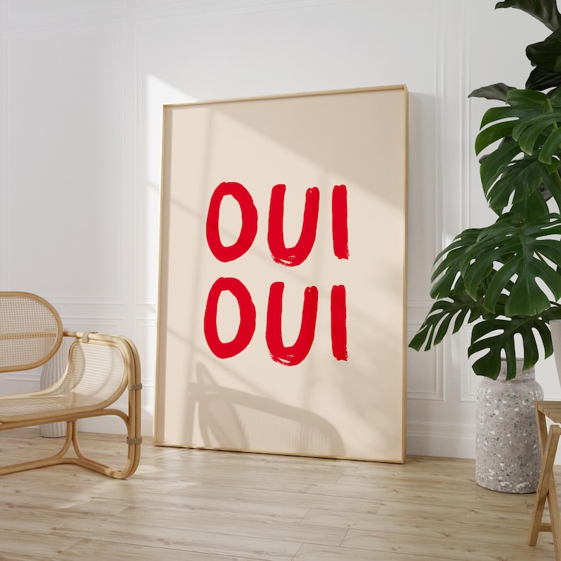 May include: A beige framed poster with the word "OUI" written twice in red paint.