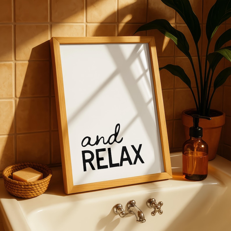 May include: A framed print with the words "and RELAX" in black script. The wooden frame sits on a bathroom sink next to a soap dish, a soap dispenser, and a potted plant. The background is a tiled wall.