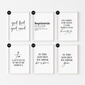 May include: Six white framed prints with black text on a white wall. The prints feature various quotes about food, drink, and life. The quotes include "good food good mood", "hoptimistic", "I'm sorry for what I said when I was hungry", "If tea can't fix it, it must be serious", "In this kitchen we drink bourbon", and "In this kitchen we drink gin".