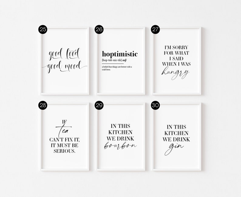 May include: Six white framed prints with black text on a white wall. The prints feature various quotes about food, drink, and life. The quotes include "good food good mood", "hoptimistic", "I'm sorry for what I said when I was hungry", "If tea can't fix it, it must be serious", "In this kitchen we drink bourbon", and "In this kitchen we drink gin".