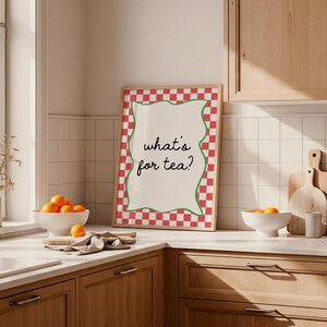 Peut inclure: Une affiche encadr&eacute;e avec le texte "what's for tea ?" dans une cuisine. L'affiche a une bordure &agrave; carreaux rouges et blancs avec un contour vert ondul&eacute;. Des oranges sont dans un bol blanc sur le comptoir.