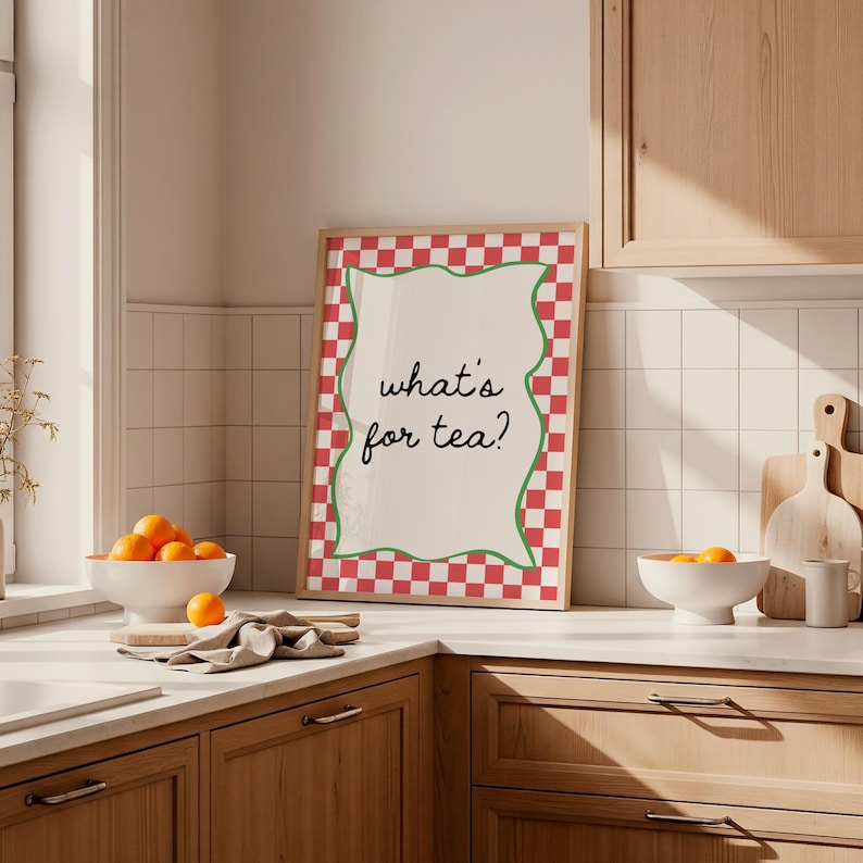 Peut inclure: Une affiche encadr&eacute;e avec le texte "what's for tea ?" dans une cuisine. L'affiche a une bordure &agrave; carreaux rouges et blancs avec un contour vert ondul&eacute;. Des oranges sont dans un bol blanc sur le comptoir.