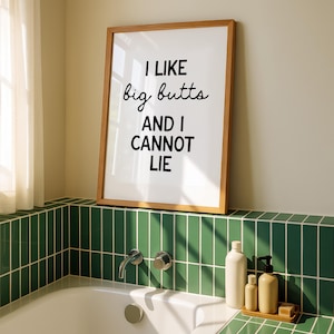 May include: A framed print with the text "I LIKE big butts AND I CANNOT LIE" in black font. The print is in a light brown wooden frame and is displayed above a bathtub with green tile.
