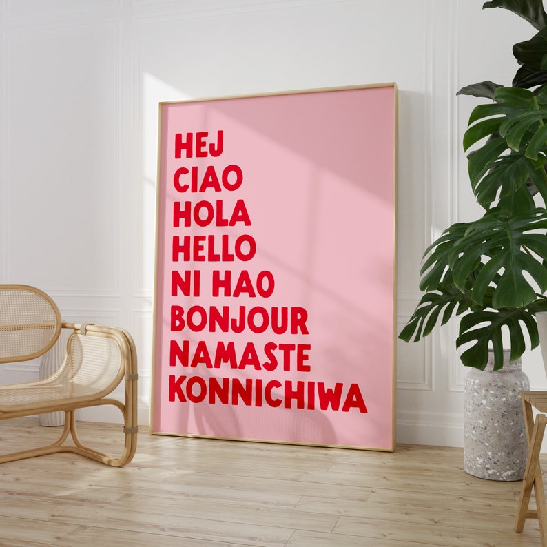 Peut inclure: Une affiche rose avec les mots "Hej", "Ciao", "Hola", "Hello", "Ni Hao", "Bonjour", "Namaste", et "Konnichiwa" &eacute;crits en rouge.