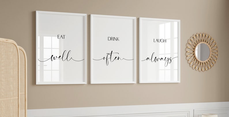 May include: Three white framed prints with black text on a beige wall. The prints read "Eat well", "Drink often", and "Laugh always".