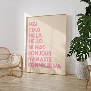 Peut inclure: Une affiche beige avec un cadre dor&eacute; pr&eacute;sentant les mots "Hej", "Ciao", "Hola", "Hello", "Ni Hao", "Bonjour", "Namaste" et "Konnichiwa" en lettres roses.