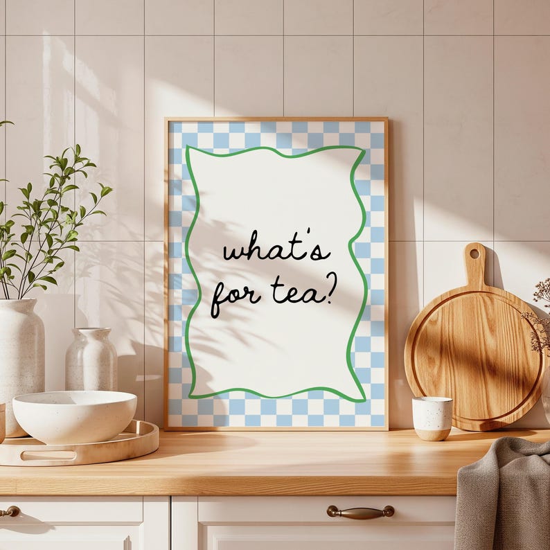Peut inclure: Une affiche encadr&eacute;e avec le texte "what's for tea ?" dans une police fantaisiste. L'affiche a un fond blanc avec une bordure verte ondul&eacute;e et un motif &agrave; carreaux bleu et blanc. Elle est pos&eacute;e sur un comptoir en bois.
