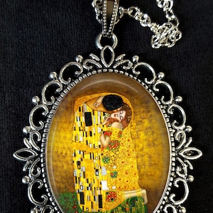 May include: A silver pendant necklace with an oval-shaped glass cameo featuring a painting of two figures embracing. The painting is in a style reminiscent of Gustav Klimt's "The Kiss".