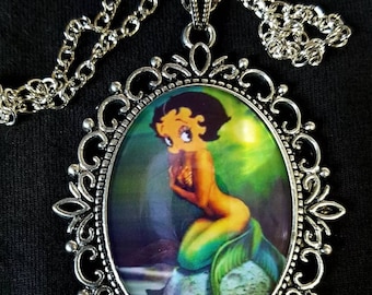 May include: A silver necklace with a cameo pendant featuring a cartoon mermaid with green hair and a tail. The cameo is set in an ornate silver frame.