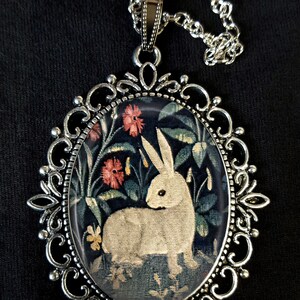 Può includere: Una collana con un ciondolo d'argento e un cammeo rotondo di vetro con un coniglio bianco in un design di arazzo floreale.