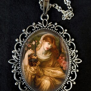 May include: A silver necklace with an oval pendant featuring a painting of a woman holding a lyre. The woman has long red hair and is wearing a gold dress. The pendant is surrounded by a decorative silver frame.