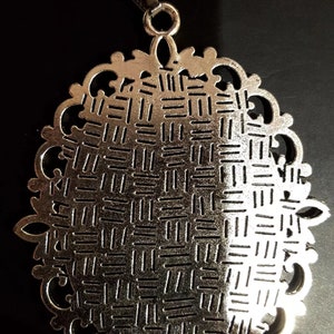 May include: Silver pendant necklace with a detailed, ornate oval design. The pendant has a textured, woven pattern.