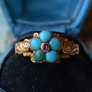 Puede incluir: Un anillo de oro con un diseño de flor de turquesa y rubí. El anillo está en una caja de anillo de terciopelo azul.