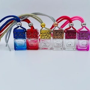 May include: Seven small glass bottles with decorative metal caps and colorful liquids. Each bottle has a string attached and a label with the text "Secret Trend" and a scent name. The scents are Mahogany Teakwood, Baja Cactus, Baja Cactus, Mahogany Teakwood, Vanilla, and Love Spell.