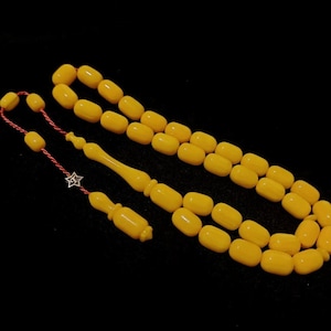May include: A yellow amber prayer beads necklace with a red string and a silver charm.