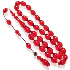 Könnte beinhalten: Eine rote Bernstein-Gebetskette mit Quaste. Die Perlen sind oval geformt und haben eine glänzende Oberfläche.