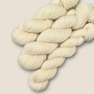 May include: Three skeins of off-white yarn, twisted together in a pile.