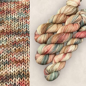 May include: A skein of variegated yarn in beige, brown, pink, and teal. The yarn is tightly wound and appears soft. The image also shows a knitted swatch of the same yarn, displaying the stitch pattern. The yarn is suitable for knitting or crochet.