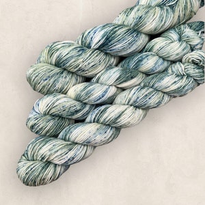 May include: A skein of yarn in a green and white colorway with speckles of blue. The yarn is soft and fluffy and would be perfect for knitting or crocheting.