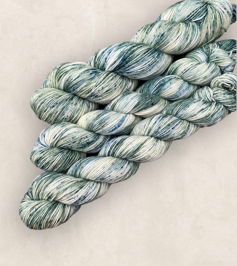May include: A skein of yarn in a green and white colorway with speckles of blue. The yarn is soft and fluffy and would be perfect for knitting or crocheting.