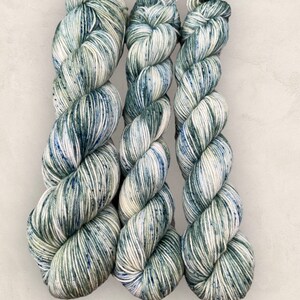 May include: Three skeins of yarn in a green and white speckled pattern. The yarn is wound into a ball shape and is ready to be used for knitting or crocheting.