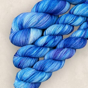 May include: A skein of blue hand-dyed yarn, with a gradient from light to dark indigo. The yarn is tightly twisted, displaying subtle colour and texture variations. Suitable for knitting or crochet.