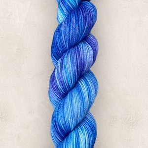 May include: A skein of blue yarn, with a gradient of shades from light to dark. The yarn is tightly twisted, giving it a textured look. This yarn is suitable for knitting or crochet projects.