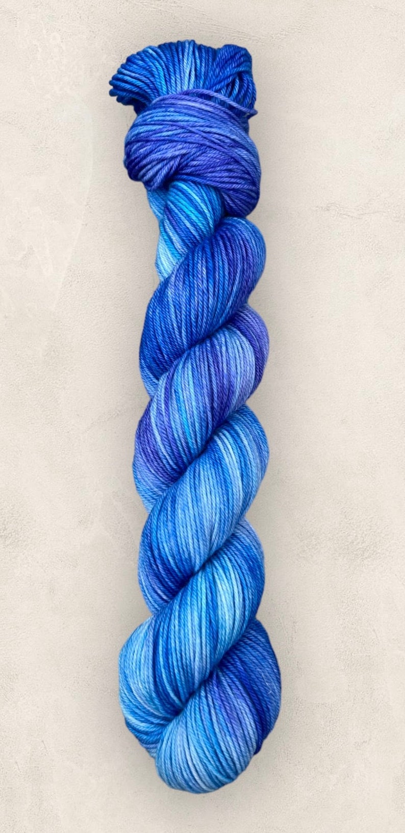 May include: A skein of blue yarn, with a gradient of shades from light to dark. The yarn is tightly twisted, giving it a textured look. This yarn is suitable for knitting or crochet projects.