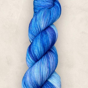 May include: A skein of blue yarn, with a mix of light and dark blues. The yarn is twisted, suggesting it's soft and suitable for knitting or crochet. The colour variation gives a visually pleasing effect.