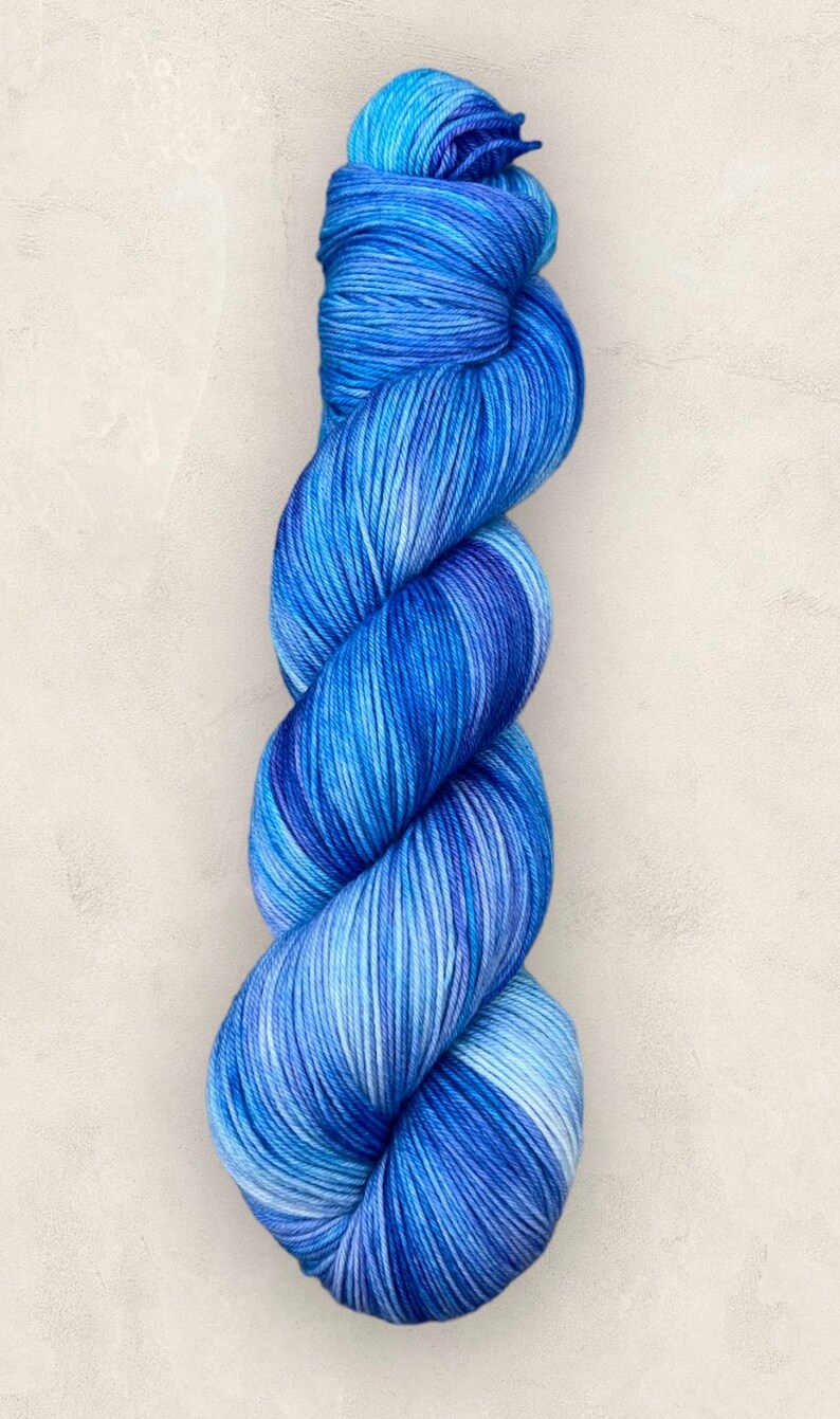 May include: A skein of blue yarn, with a mix of light and dark blues. The yarn is twisted, suggesting it's soft and suitable for knitting or crochet. The colour variation gives a visually pleasing effect.