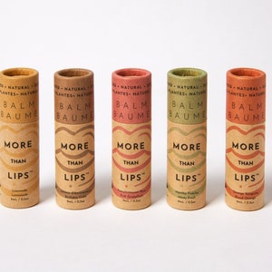 Könnte beinhalten: Fünf Pappröhrchen mit Lippenbalsam mit dem Text "More Than Lips" und verschiedenen Geschmacksrichtungen: Limonade, Citrus of Innocence Birthday Cake, Granatapfel-Rose Pink Grapefruit, Minzig Frisch Minze Birke und Orangen-Sorbet Blutorange.