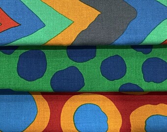 May include: Three fabric swatches with different geometric patterns. The top swatch has a chevron pattern in shades of blue, green, orange, and red. The middle swatch has a green background with blue polka dots. The bottom swatch has a red background with orange circles and blue polka dots.