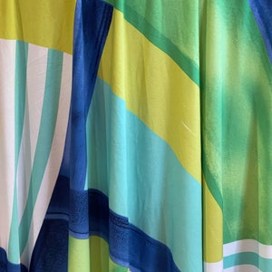 May include: Abstract fabric with a geometric pattern in shades of blue, green, and yellow. The fabric has a flowing, draped look.