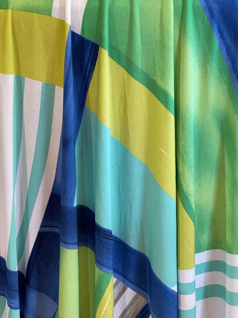 May include: Abstract fabric with a geometric pattern in shades of blue, green, and yellow. The fabric has a flowing, draped look.