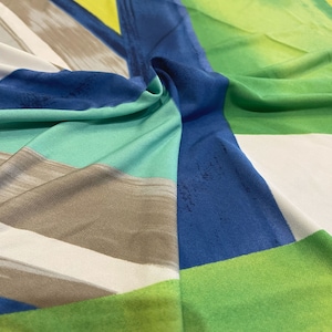 May include: Abstract geometric fabric with a blue, green, white, and brown color scheme. The fabric has a smooth, silky texture.