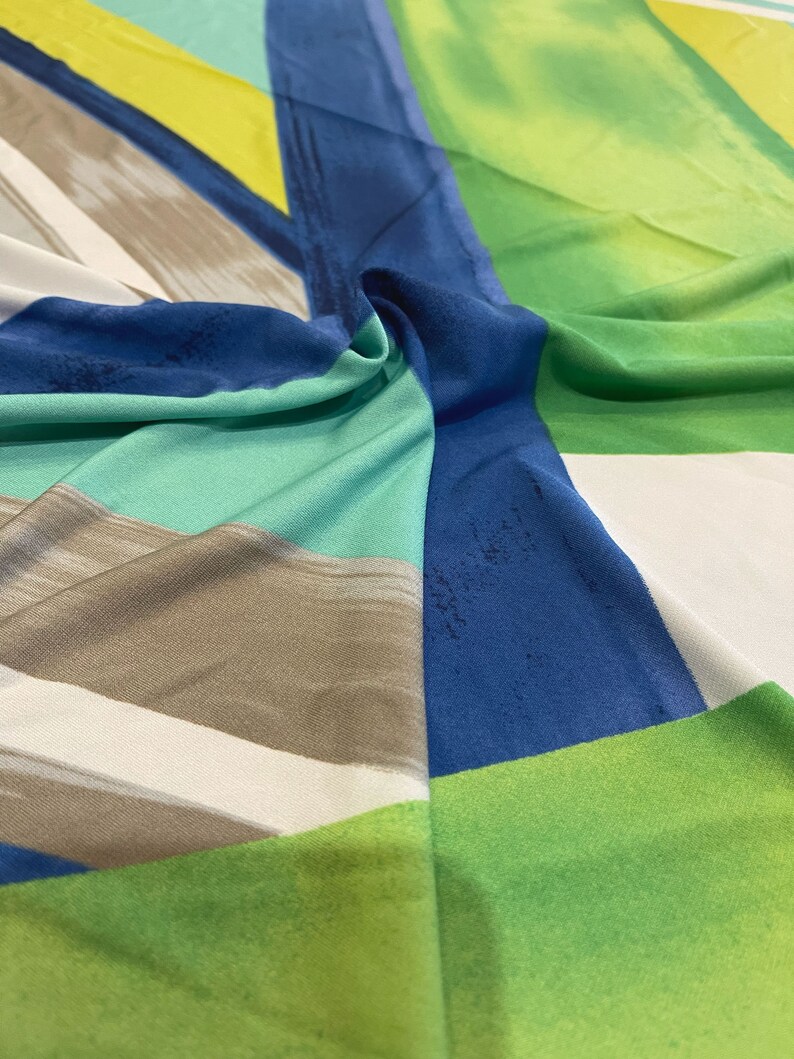 May include: Abstract geometric fabric with a blue, green, white, and brown color scheme. The fabric has a smooth, silky texture.