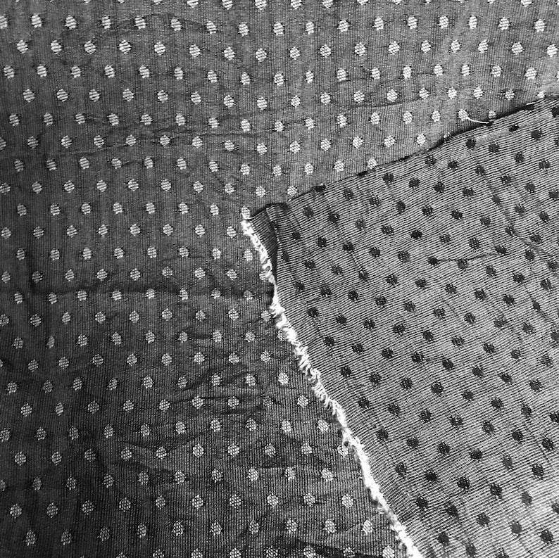 May include: Black and white fabric with a polka dot pattern. The fabric is textured and has a slightly rough feel.