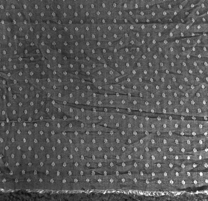May include: A close-up of a black fabric with a white polka dot pattern. The fabric has a textured surface and a slightly wrinkled appearance.