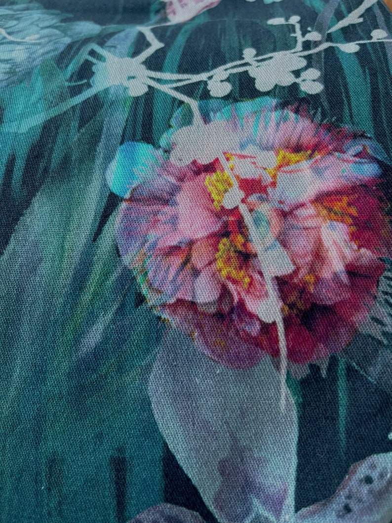 Pode incluir: Close-up de um tecido floral com uma flor rosa e roxa com um centro amarelo. O tecido tem um fundo verde e preto com um padr&atilde;o floral branco.