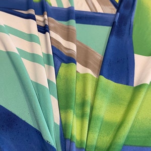 May include: Abstract fabric with a colorful geometric pattern in shades of blue, green, white, and yellow. The fabric has a smooth, silky texture.