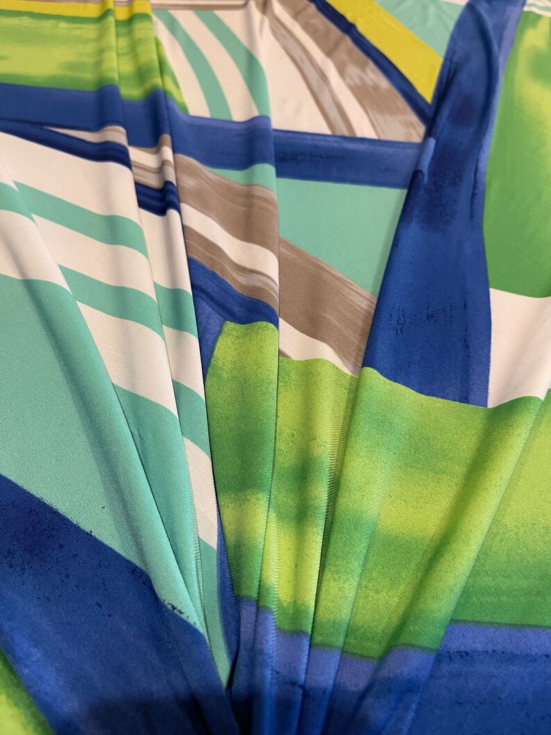 May include: Abstract fabric with a colorful geometric pattern in shades of blue, green, white, and yellow. The fabric has a smooth, silky texture.