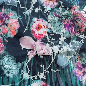Pode incluir: Um tecido azul escuro com uma estampa floral com flores rosa, brancas e verdes. As flores s&atilde;o estilizadas e t&ecirc;m um efeito aquarela.