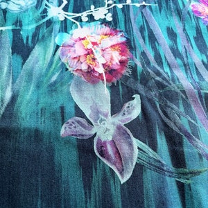 Pode incluir: Um tecido turquesa com estampa floral com flores rosa e roxas. O tecido tem um aspecto texturizado e tecido.