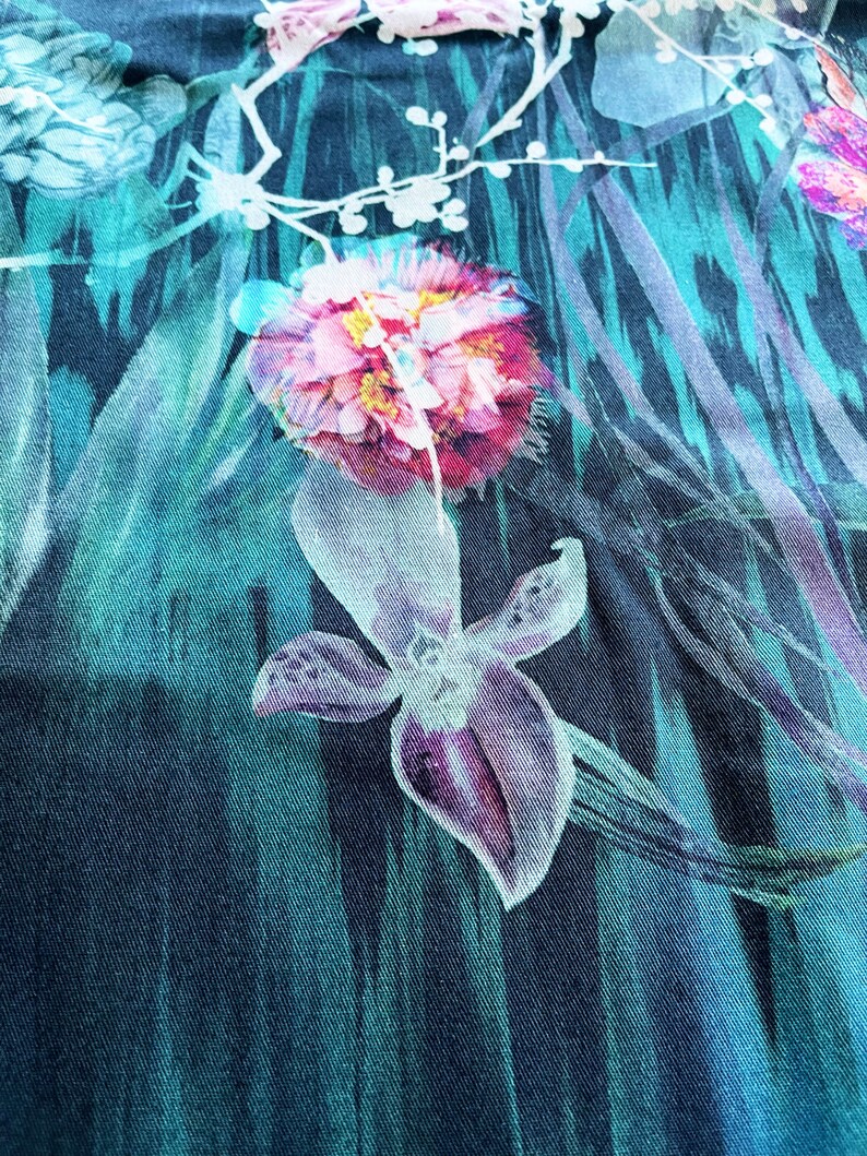 Pode incluir: Um tecido turquesa com estampa floral com flores rosa e roxas. O tecido tem um aspecto texturizado e tecido.