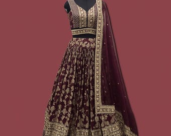 May include: A burgundy lehenga choli set with detailed gold embroidery. The set comprises a sleeveless top, a flared skirt, and a matching dupatta. The embroidery showcases floral and geometric patterns, creating a luxurious appearance. The outfit is displayed on a mannequin.