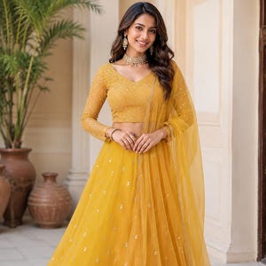 May include: A mustard yellow lehenga choli set featuring a long-sleeved blouse with intricate embroidery and a matching floor-length skirt with scattered sequin embellishments. A sheer, lightweight dupatta with a decorative border completes the outfit.