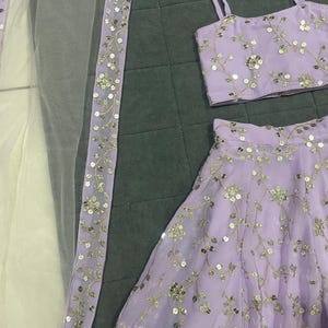 May include: A lilac-colored three-piece outfit with silver embroidery. The outfit includes a sleeveless top, a skirt, and a sheer dupatta with a silver border.
