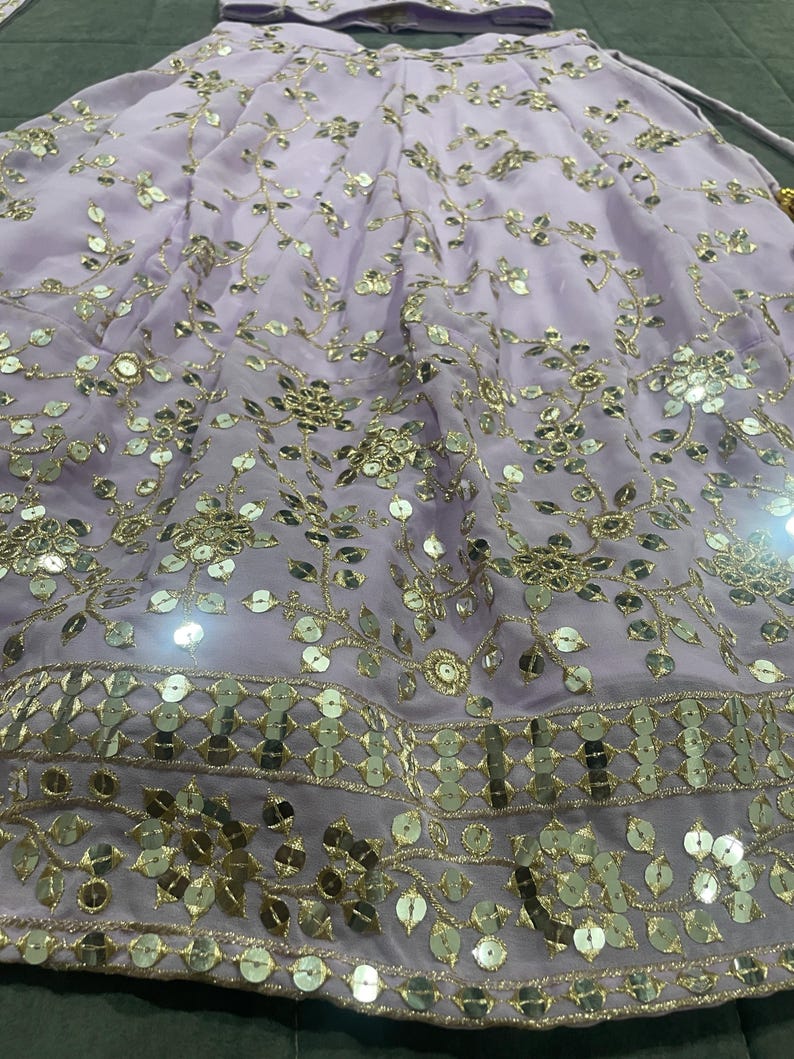 May include: A lavender skirt with gold embroidery and sequins. The skirt has a floral pattern and a layered design.