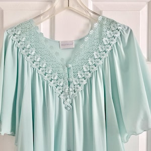 May include: A light mint green nightgown featuring a V-neckline adorned with intricate white floral lace trim. The garment has short, flared sleeves and a front button placket with matching fabric-covered buttons. A label reads Shadowline.